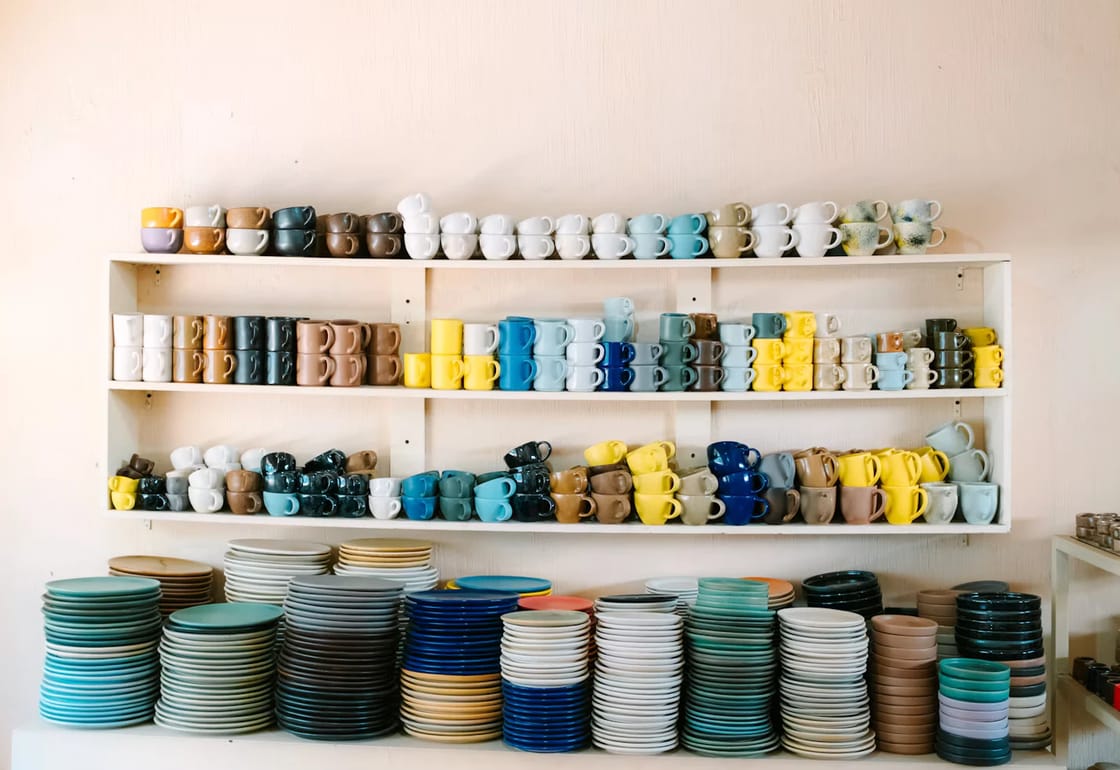 Shelves stacked with colourful cups, mugs and plates ready for events
